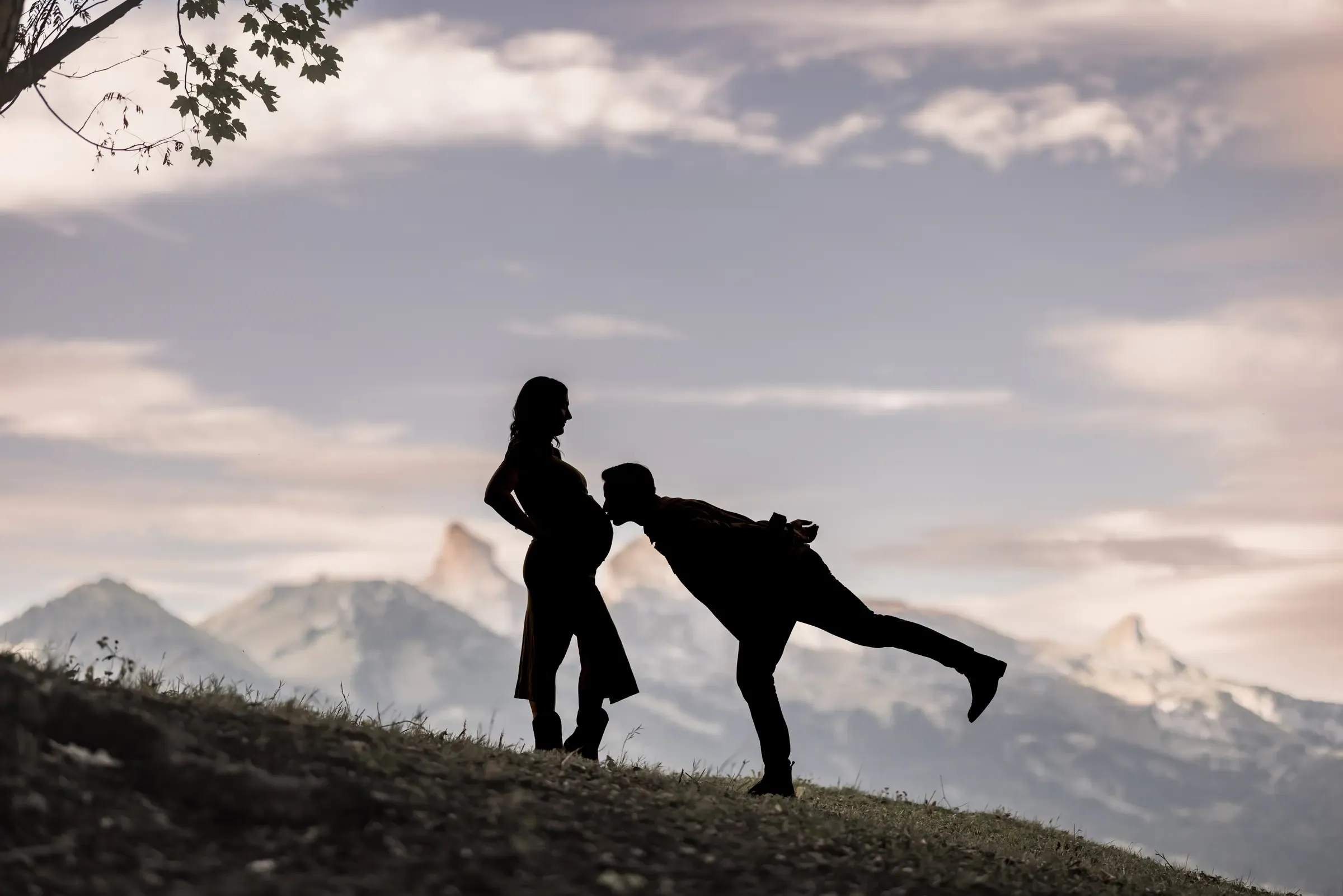 Silhouette d'un couple face aux montagnes, le futur papa penché vers le ventre