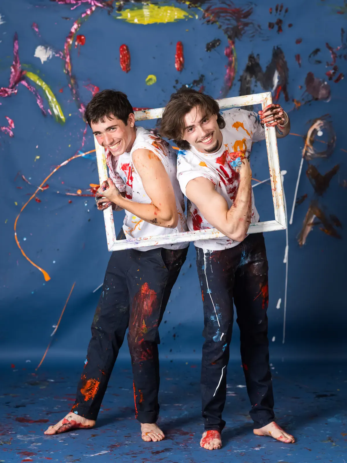Deux jeunes hommes couverts de peinture tiennent un cadre vide, sur fond bleu